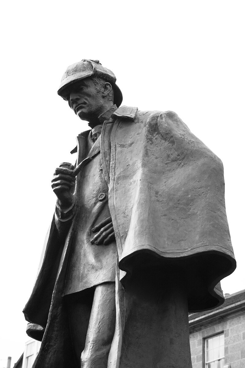 Bronze statue of a man in a cap and long coat, looking downward and gripping his lapel.