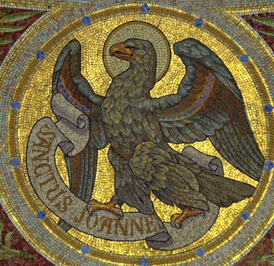 Gold mosaic depicting a crowned eagle with halo and spread wings, gripping a scroll that reads 'SANCTUS IOANNES' against a radiant circular background.